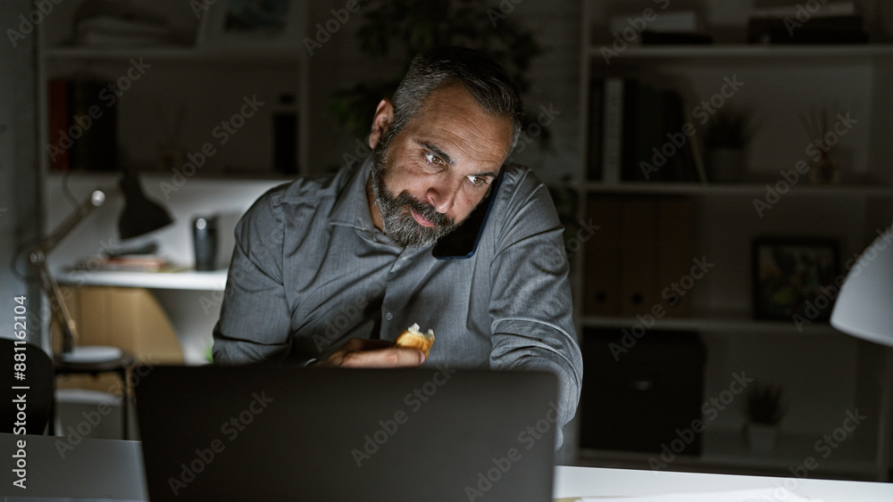 Mature hispanic man with grey beard working late in dark office interior. Mature hispanic man with grey beard working late in dark office interior.