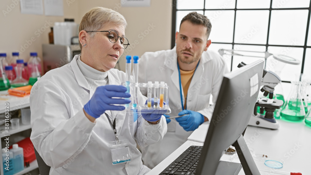 Man and woman scientists in lab conducting research with test tubes and computer Man and woman scientists in lab conducting research with test tubes and computer