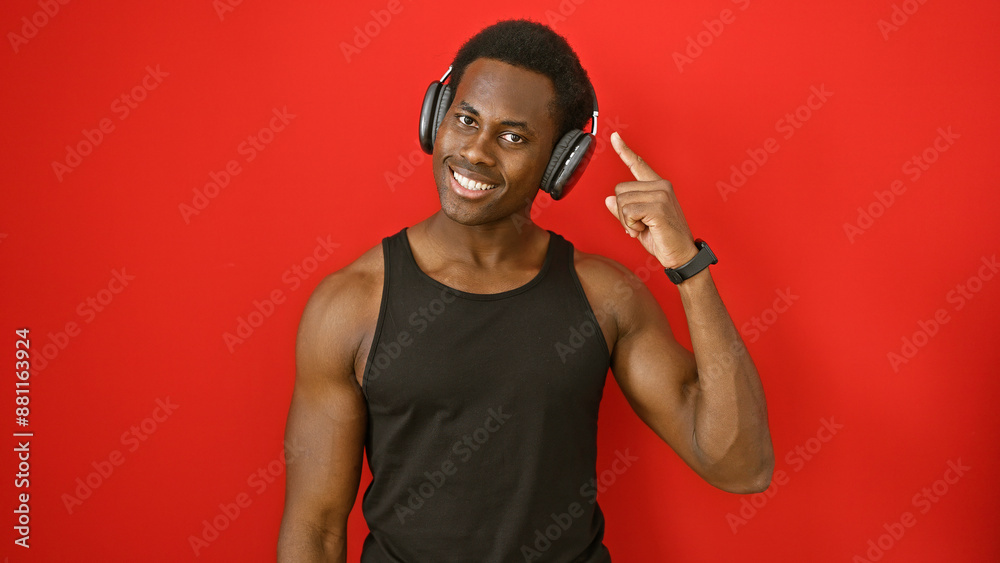 Smiling african american man in black tank top wearing headphones and pointing to his head against a red background. Smiling african american man in black tank top wearing headphones and pointing to his head against a red background.