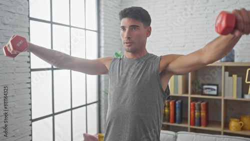 Handsome hispanic man exercising with dumbbells in a modern living room, focused and fit. photo