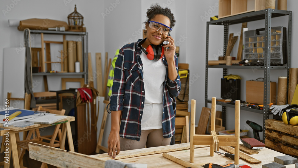 Smiling woman talking on phone in carpentry workshop with safety glasses Smiling woman talking on phone in carpentry workshop with safety glasses