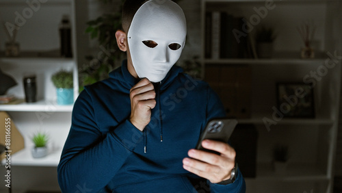 Фотография A mysterious man wearing a blank mask holds a smartphone in a modern office setting