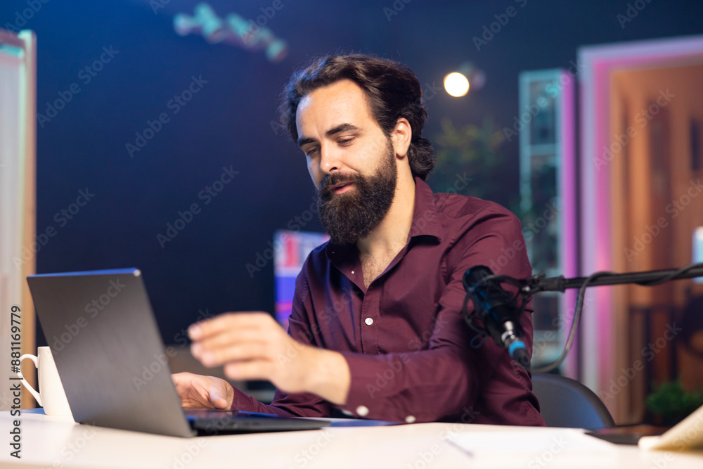 Man doing live broadcast talking to audience about recent news headlines, reading from laptop. Internet show host talking with viewers, presenting information in entertaining manner Man doing live broadcast talking to audience about recent news headlines, reading from laptop. Internet show host talking with viewers, presenting information in entertaining manner