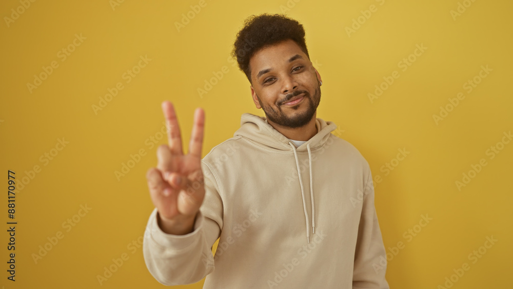 Naklejka premium Handsome black man making peace sign in beige hoodie against yellow background