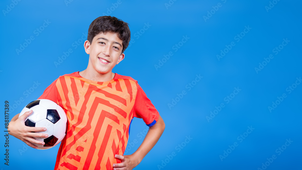 A kid is holding a soccer ball and smiling isolated on blue background with space for text. Concept of joy and sports. A kid is holding a soccer ball and smiling isolated on blue background with space for text. Concept of joy and sports.