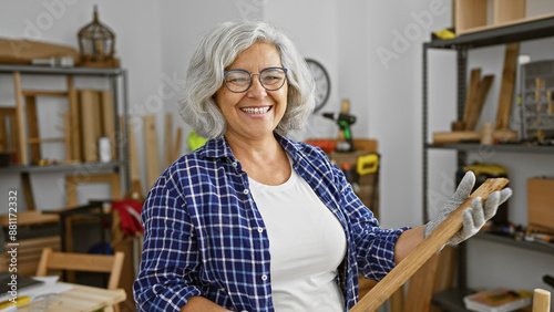 Vászonkép A cheerful mature woman in a woodworking workshop surrounded by tools and wooden furniture