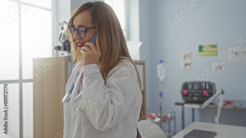 Blonde woman in a clinic discussing on the phone while wearing a white coat