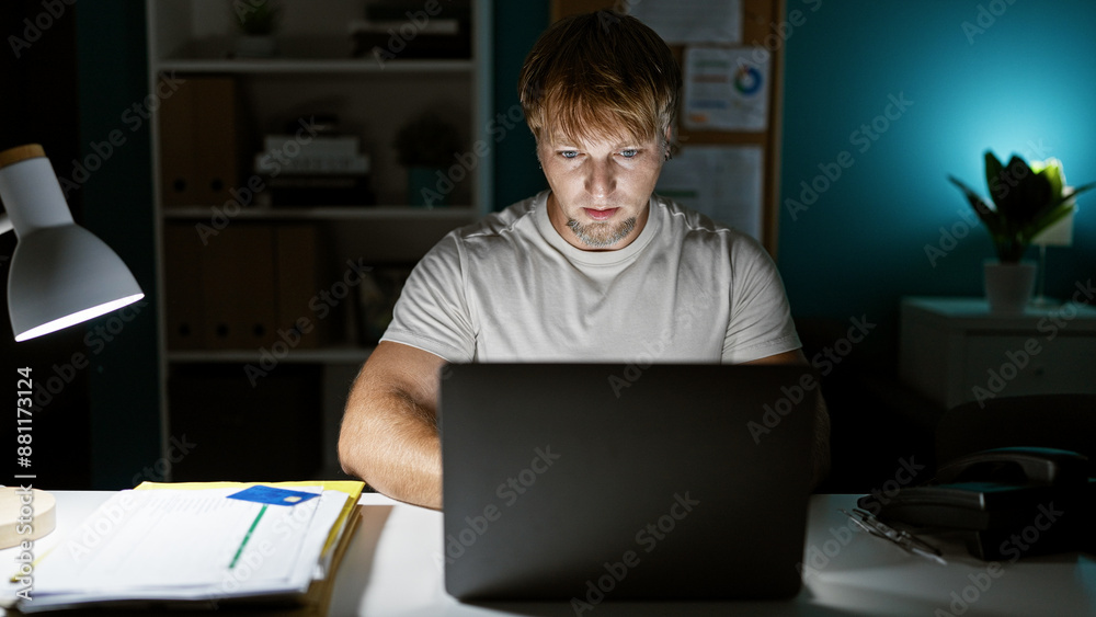 Focused young man with beard working late on laptop in modern office indoors. Focused young man with beard working late on laptop in modern office indoors.