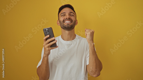 фотографія Handsome young hispanic man celebrating with smartphone over isolated yellow background