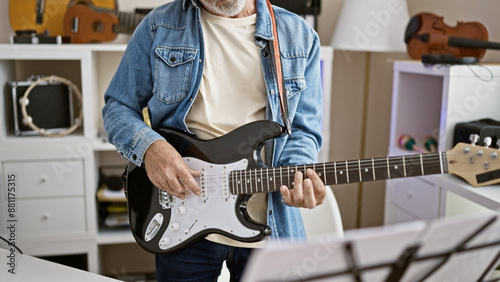 A mature man in casual attire plays an electric guitar in a modern room filled with musical instruments. photo