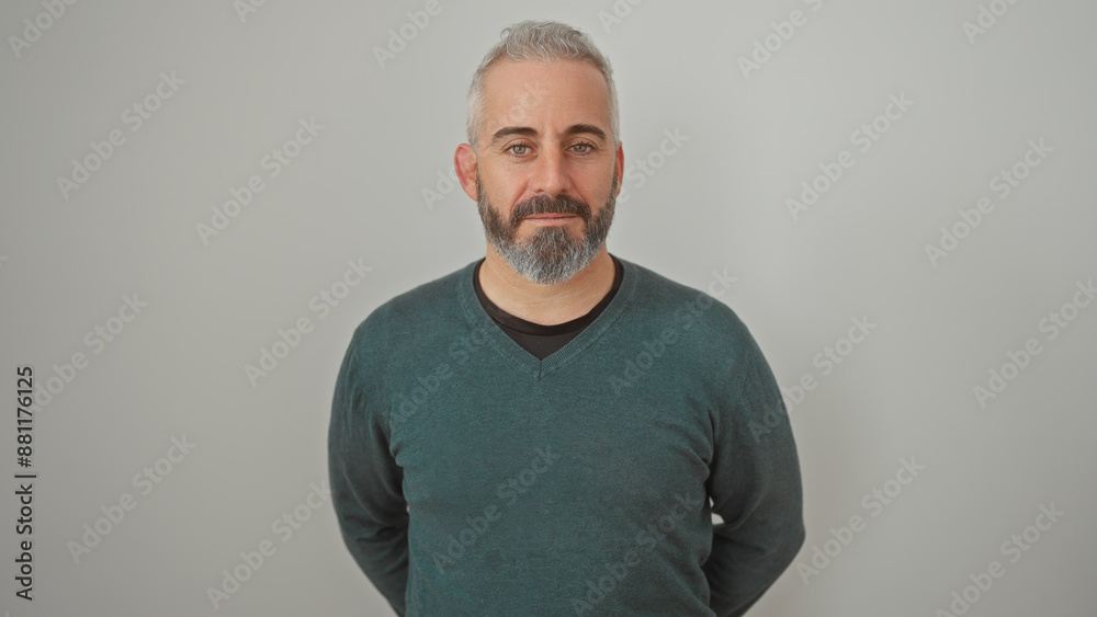 A confident, middle-aged man with a beard and casual attire stands against a plain white background. A confident, middle-aged man with a beard and casual attire stands against a plain white background.