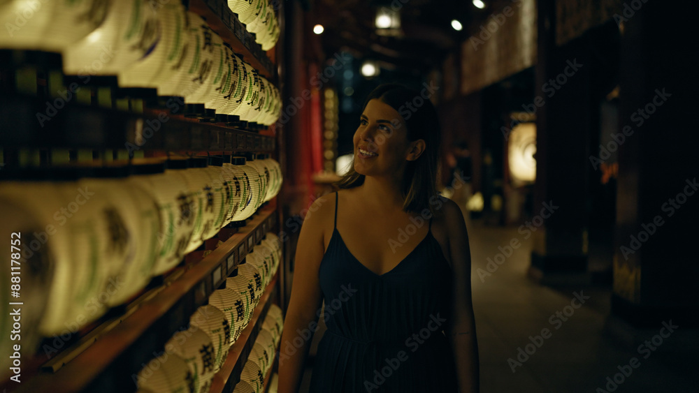 Fototapeta premium Beautiful young hispanic woman looking at asian lantern at japanese temple in tokyo at night