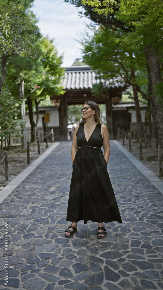 Naklejka premium Cheerful young hispanic woman, effortlessly beautiful with glasses, confidently posing and joyfully smiling while exploring the serene surroundings of ginkaku-ji temple, kyoto, japan