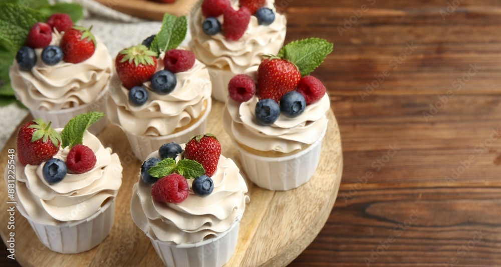 Tasty cupcakes with different berries and mint on wooden table, closeup. Space for text Tasty cupcakes with different berries and mint on wooden table, closeup. Space for text