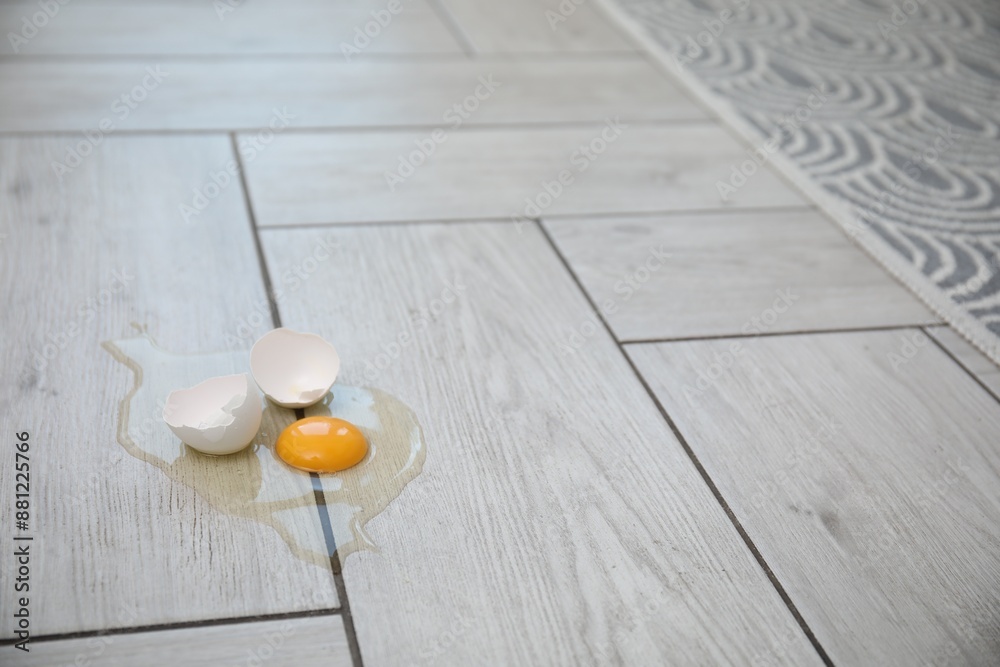 Broken raw egg and shell on light grey wooden floor indoors. Space for text Broken raw egg and shell on light grey wooden floor indoors. Space for text