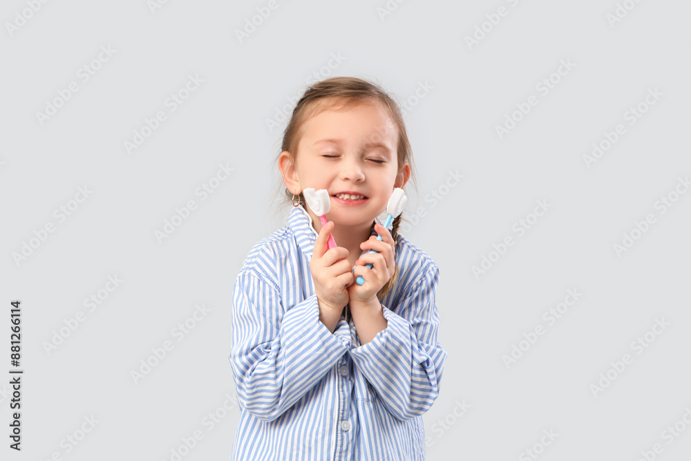 Happy little girl in pajamas with toothbrushes on grey background Happy little girl in pajamas with toothbrushes on grey background