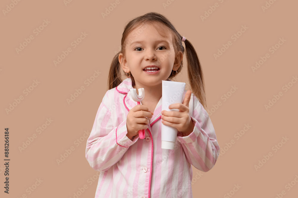 Happy little girl in pajamas with brush and toothpaste on brown background Happy little girl in pajamas with brush and toothpaste on brown background
