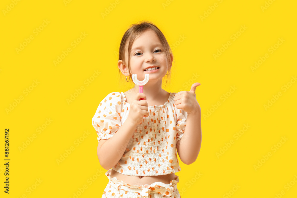 Cute little girl in pajamas with toothbrush showing thumb-up gesture on yellow background Cute little girl in pajamas with toothbrush showing thumb-up gesture on yellow background