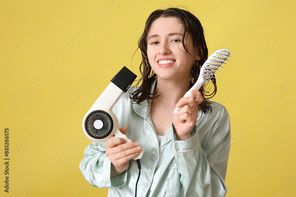 Obraz premium Beautiful young happy woman with brush and hairdryer on yellow background