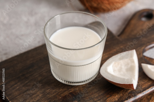 Glass of tasty fresh coconut milk and wooden cutting board on grunge background, closeup