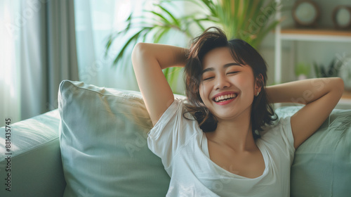 Happy Short Hair Asian Woman Dancing on Sofa at Home - Smiling Girl Enjoying Day Off Lying on Couch - Healthy Lifestyle, Good Vibes, New Home Concept