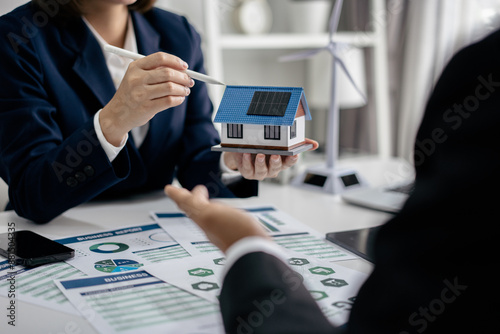 Real Estate Broker discussing with a customer model install solar roof house modern project in the office, real estate developer alternative energy, development business sustainable, zero energy, ESG.