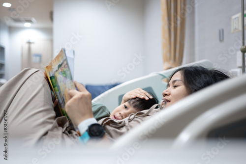 The patient mother and child read the book while lying on the hospital bed from sickness or injury.