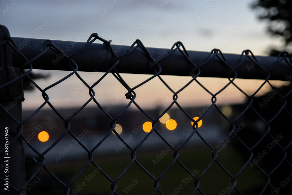Sunset bokeh lights behind chain-link fence - blurred urban background with warm glowing orbs - dusk sky gradient. Taken in Toronto, Canada. Sunset bokeh lights behind chain-link fence - blurred urban background with warm glowing orbs - dusk sky gradient. Taken in Toronto, Canada.
