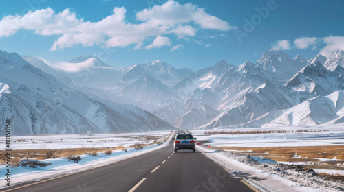 A car is driving on the road, with snow mountains behind it and blue sky above