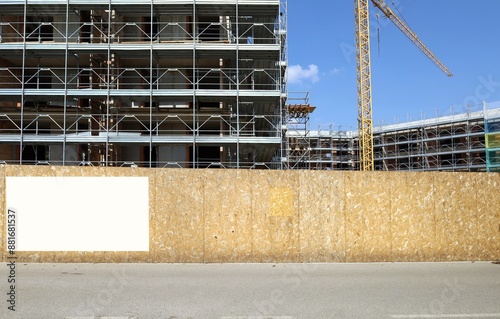 Wallpaper Mural Blank information board on fence outside the construction site with a new large building among the scaffolding, Tower crane and sky. Background for copy space. Torontodigital.ca