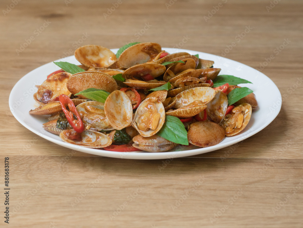 Stir fried striped clams with basil, chilli paste, garlic and fresh chilies. Placed in a white plate with a beautiful pattern and on the wood pattern background. Stir fried striped clams with basil, chilli paste, garlic and fresh chilies. Placed in a white plate with a beautiful pattern and on the wood pattern background.