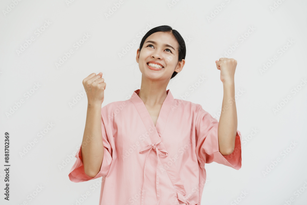 A young Asian female wearing a pink patient uniform stands isolated against a white wall background, showing confidence despite having her arm in a sling due to an injury. A young Asian female wearing a pink patient uniform stands isolated against a white wall background, showing confidence despite having her arm in a sling due to an injury.