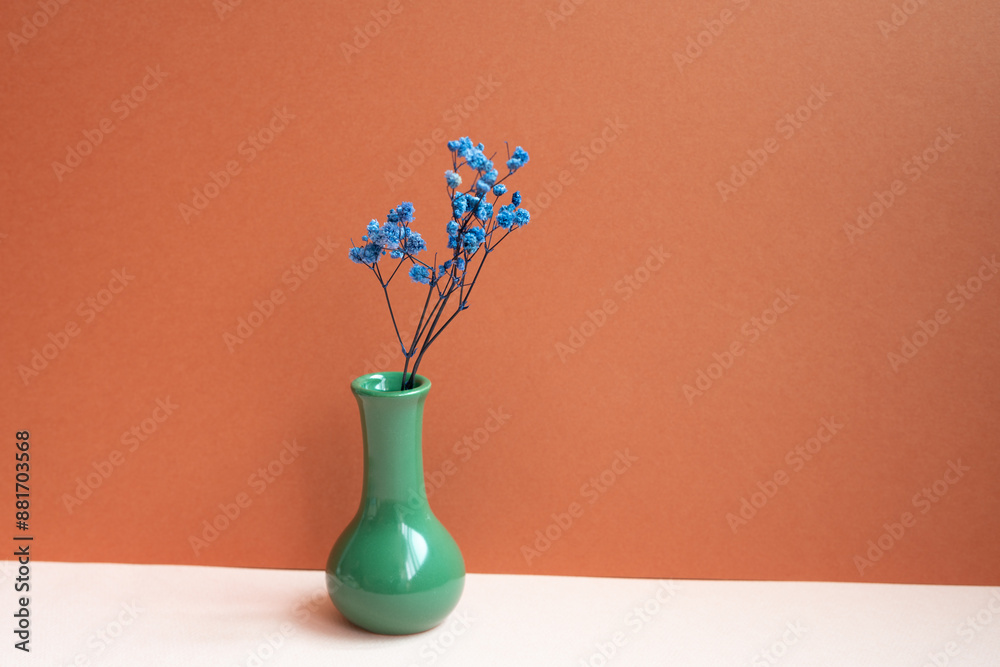 Green vase of blue dry flower on pink table. red background