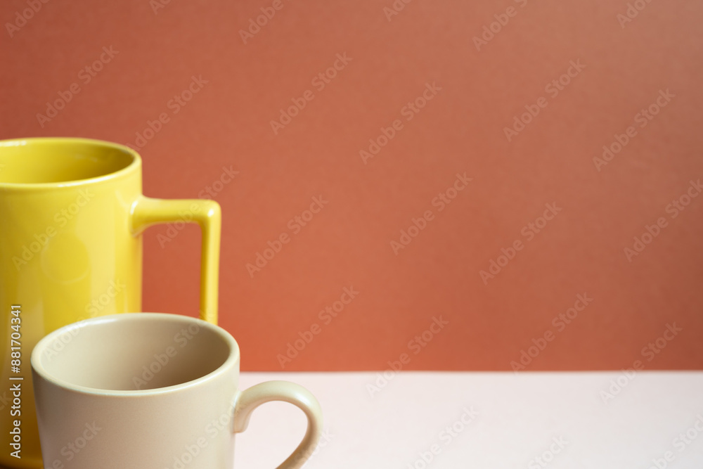 Yellow and beige mug cups on pink table. red background