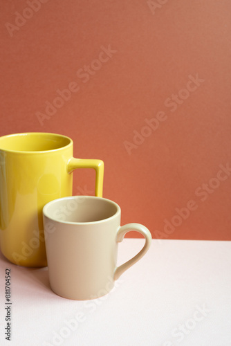 Yellow and beige mug cups on pink table. red background