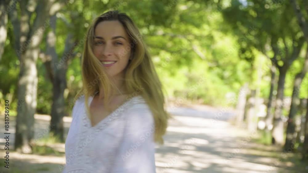 Cheerful caucasian young blonde woman in a white dress is walking in the park Cheerful caucasian young blonde woman in a white dress is walking in the park