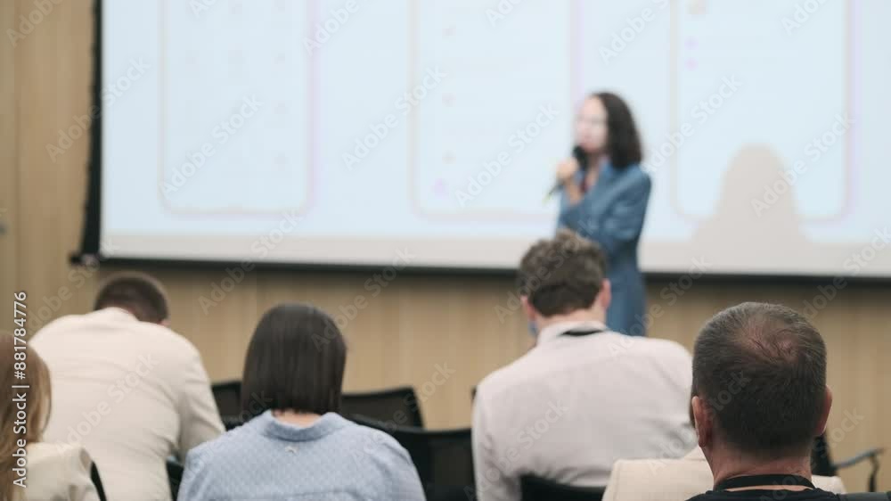 Business professional presenting mobile app features to an audience during a seminar. Focus on screen projection and attentive audience. Business professional presenting mobile app features to an audience during a seminar. Focus on screen projection and attentive audience.