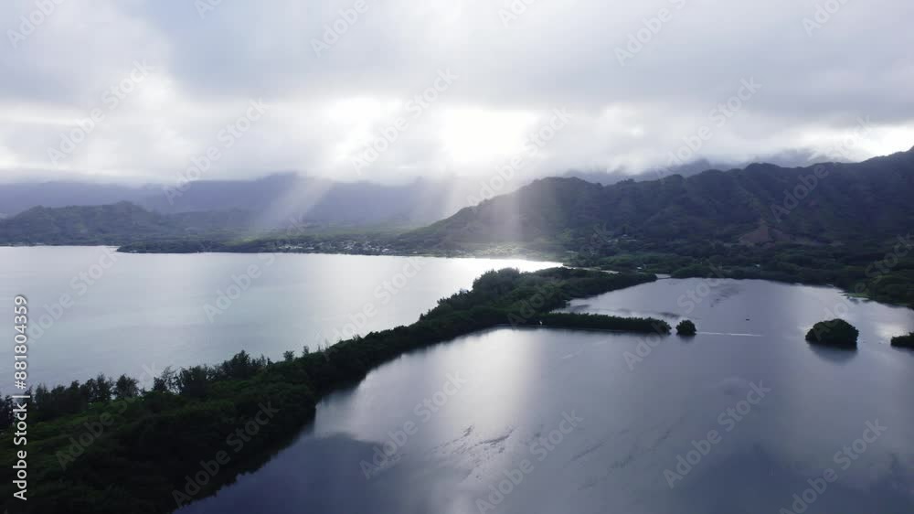 A stunning aerial view capturing the sunrays breaking through clouds over the Koolau Mountains, illuminating the serene bay and lush greenery below. A stunning aerial view capturing the sunrays breaking through clouds over the Koolau Mountains, illuminating the serene bay and lush greenery below.