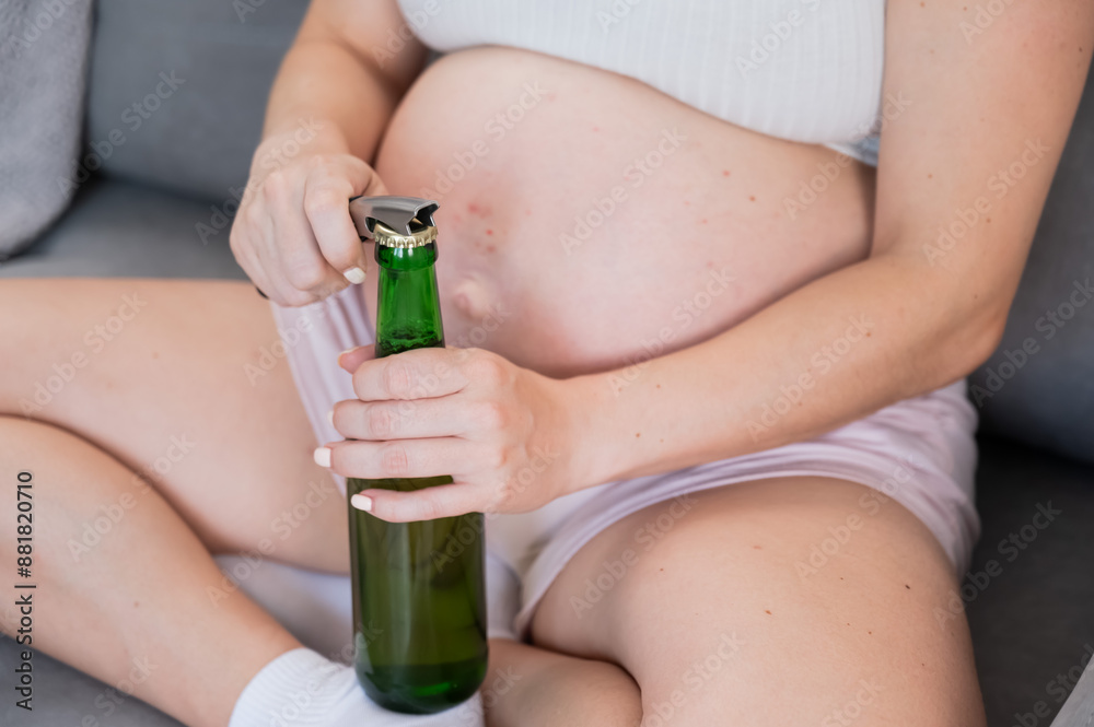 Faceless pregnant woman sitting on the sofa and opening a bottle of beer. Faceless pregnant woman sitting on the sofa and opening a bottle of beer.