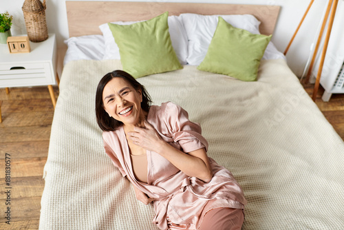 Mature woman relaxes on pink bed in cozy robe. photo