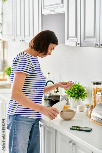 A woman in cozy attire stands in a kitchen, preparing food with focus and skill.