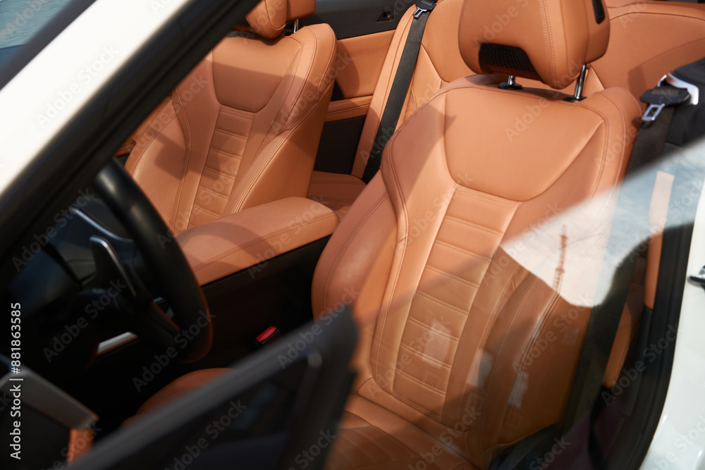 Obraz premium A view of the driver's seat in a white convertible car with a brown interior, parked on the street.