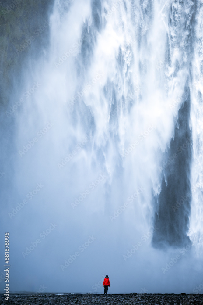Stunning view of the Skógafoss Waterfall with a tourist wearing a red jacket. Skógafoss is one of the biggest waterfalls in Iceland, situated on the Skoga River in the south of Iceland.