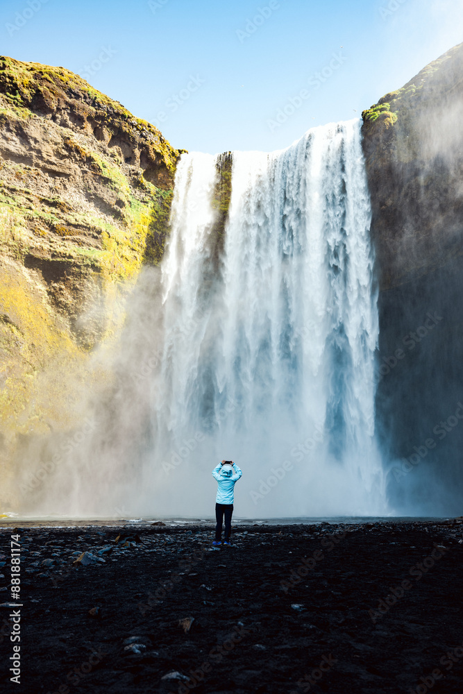 Stunning view of the Skógafoss Waterfall with a tourist taking pictures. Skógafoss is one of the biggest waterfalls in Iceland, situated on the Skoga River in the south of Iceland.