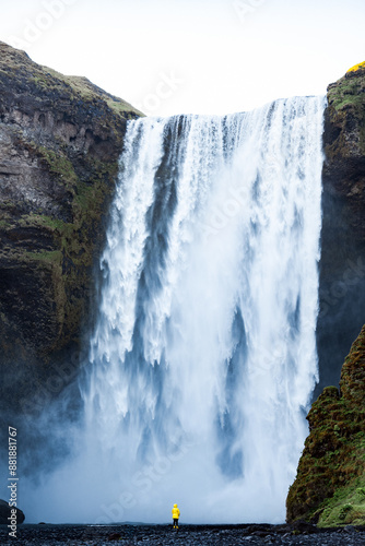 Obraz na płótnie Stunning view of the Skógafoss Waterfall with a tourist wearing a yellow jacket. Skógafoss is one of the biggest waterfalls in Iceland, situated on the Skoga River in the south of Iceland. w salonie