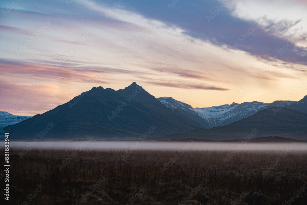 Stunning view of a dramatic landscape with some snowy mountains and a glacier in the distance during a beautiful sunrise, Iceland.