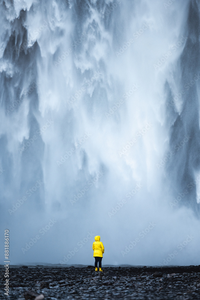 Stunning view of the Skógafoss Waterfall with a tourist wearing a yellow jacket. Skógafoss is one of the biggest waterfalls in Iceland, situated on the Skoga River in the south of Iceland.