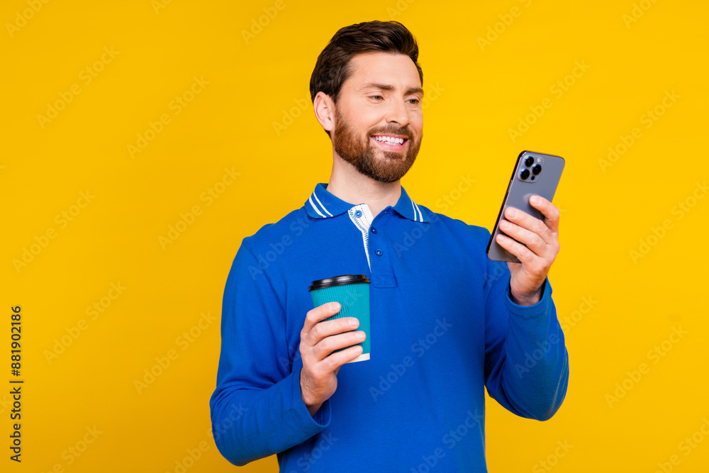 Photo portrait of handsome young guy drink coffee hold gadget dressed stylish blue garment isolated on yellow color background Photo portrait of handsome young guy drink coffee hold gadget dressed stylish blue garment isolated on yellow color background