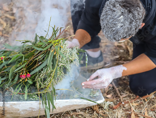 Human hands with green branches, wooden ritual dish and fire, Australian aboriginal smoking ceremony, indigenous event