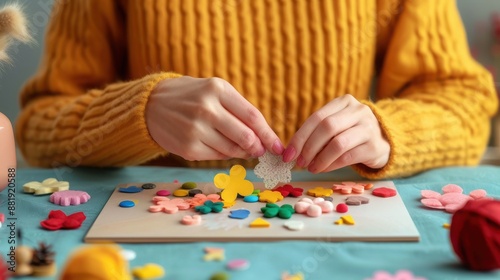 Close-up of person in yellow sweater crafting with colorful paper pieces on a blue table, creating a vibrant and creative handmade design.